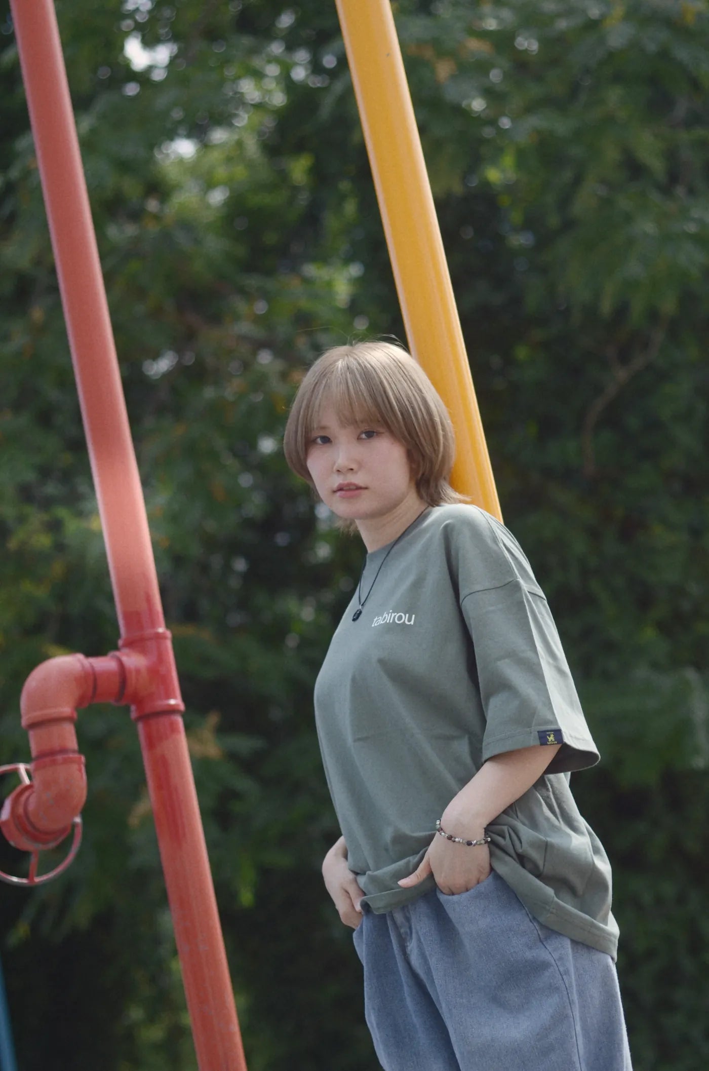 赤い配管の前に立つ、モスグリーンのビッグTシャツの全身